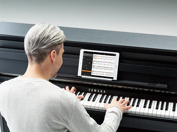 Hombre tocando piano CLP con partituras en una tablet.